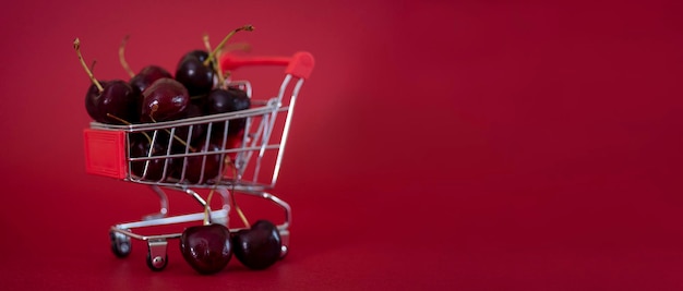 Un mini carrello da supermercato in metallo pieno di succose ciliegie rosse su uno spazio di copia di sfondo bardico