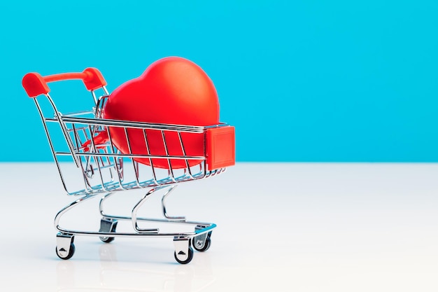 Un mini carrello della spesa a forma di cuore rosso su sfondo blu per studio Concetto di amore di San Valentino Il concetto di conservazione della salute