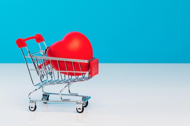 Un mini carrello della spesa a forma di cuore rosso su sfondo blu per studio Concetto di amore di San Valentino Il concetto di conservazione della salute