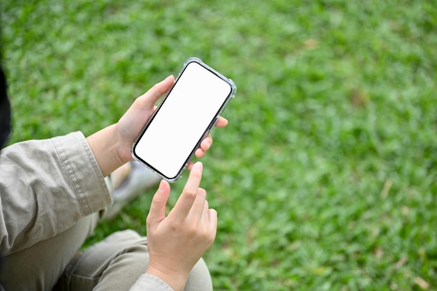 Un mockup di smartphone è nella mano di una donna su uno sfondo sfocato di erba verde