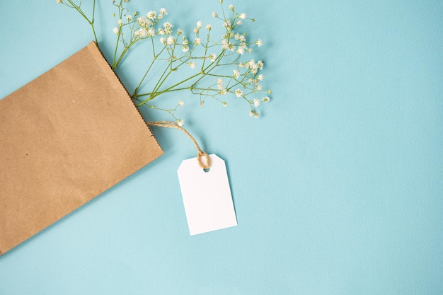 Un mockup di un'etichetta bianca e un cartellino del prezzo vicino a un pacchetto artigianale con fiori si trovano su un tavolo blu