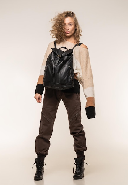Un modello con un maglione marrone a righe e cargo pubblicizza uno zaino in pelle nera