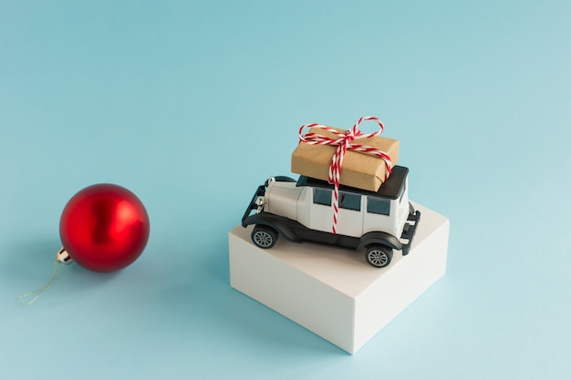 Un modello di auto retrò con una scatola di Natale sul tetto su un podio bianco e uno sfondo blu con una palla di Natale rossa.