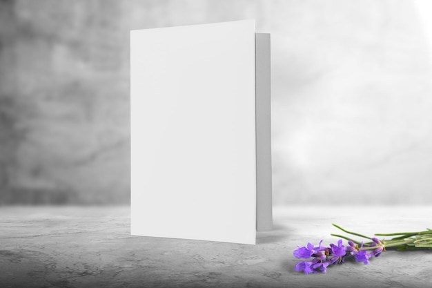 Un modello di biglietto di auguri bianco, in piedi su una scrivania di legno bianca con fiori