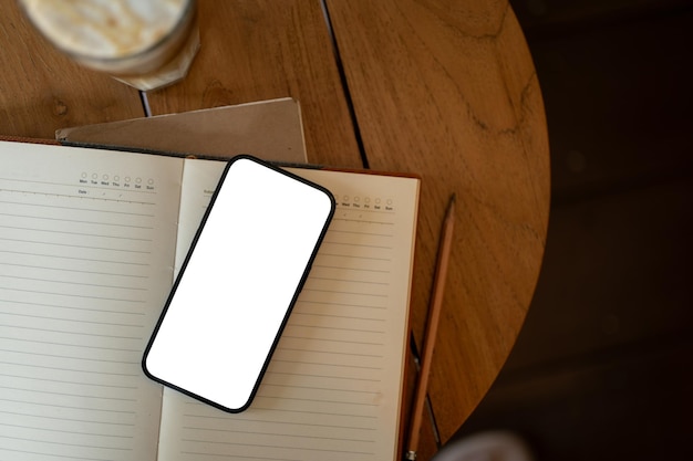 Un modello di smartphone con schermo bianco su un libro aperto su un tavolo di legno in una caffetteria