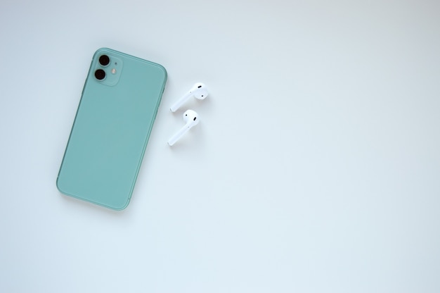 Un moderno smartphone color menta con cuffie wireless su bianco. Lay piatto