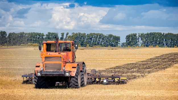 Un moderno trattore arancione ara il campo di grano dorato della terra