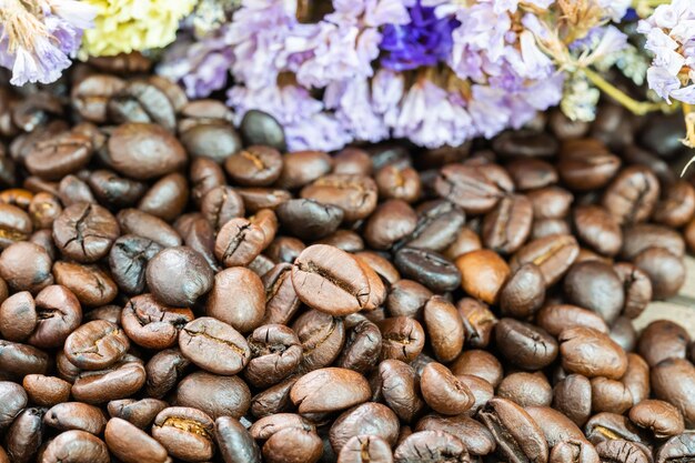 Un mucchio di chicchi di caffè tostati da vicino con uno sfondo di fiori