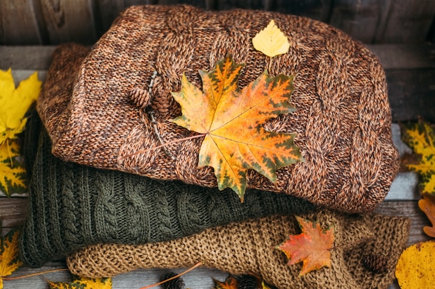 Un mucchio di maglioni caldi su un tavolo di legno con foglie di autunno