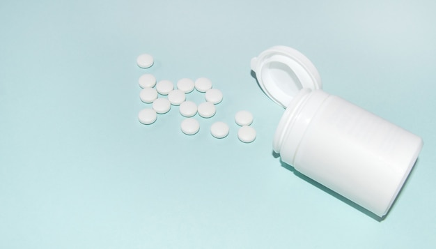 Un mucchio di pillole giaceva davanti a una piccola bottiglia di plastica aperta su uno sfondo azzurro, uno striscione