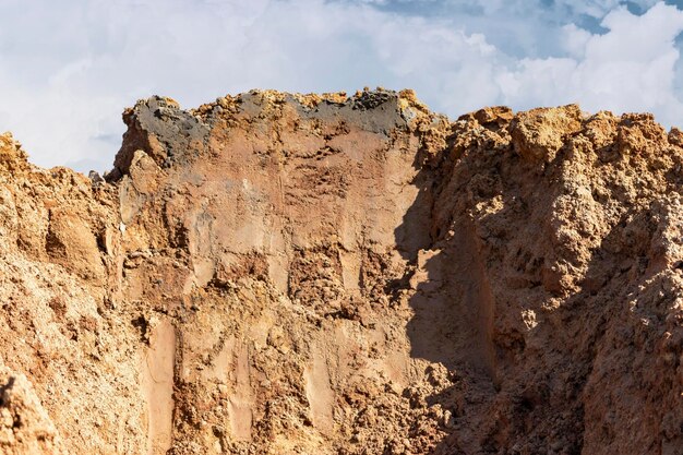 Un mucchio di terreno scavato da una trincea contro un cielo nuvoloso blu Lavori di sterro al cantiere