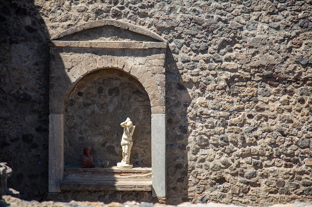 Un muro di pietra con una statua al centro nell'antica città di Pompei