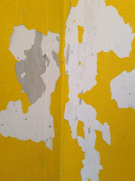 Un muro giallo con vernice scrostata e un muro bianco che è stato dipinto nell'angolo.