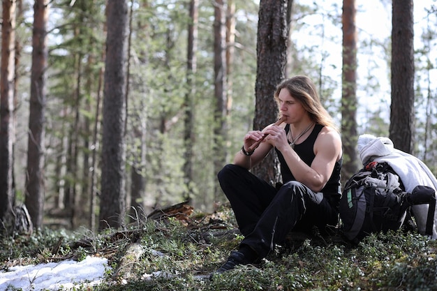 Un musicista con uno strumento in natura. L'uomo sta suonando un flauto in una pineta. La musica dei druidi nella foresta primaverile.