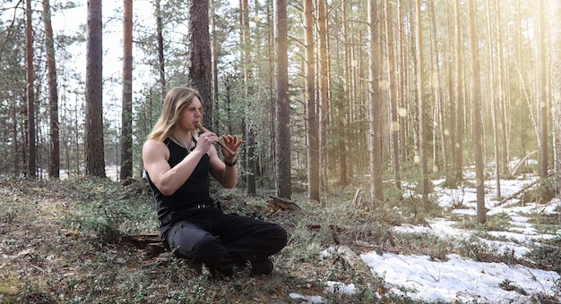 Un musicista con uno strumento nella natura L'uomo suona un flauto in una pineta La musica dei druidi in primavera forestxA