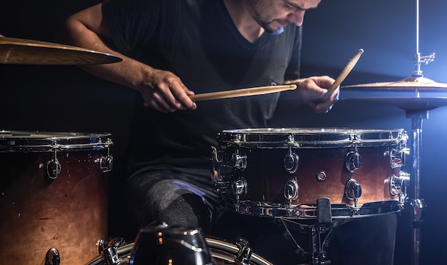 Un musicista suona la batteria con le bacchette sul palco con l'illuminazione del palco.