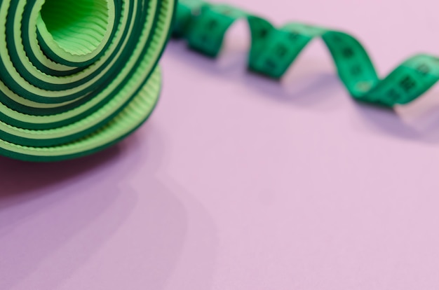 Un nastro di misurazione verde ritorto a spirale e un tappetino per il fitness si trovano su uno sfondo viola