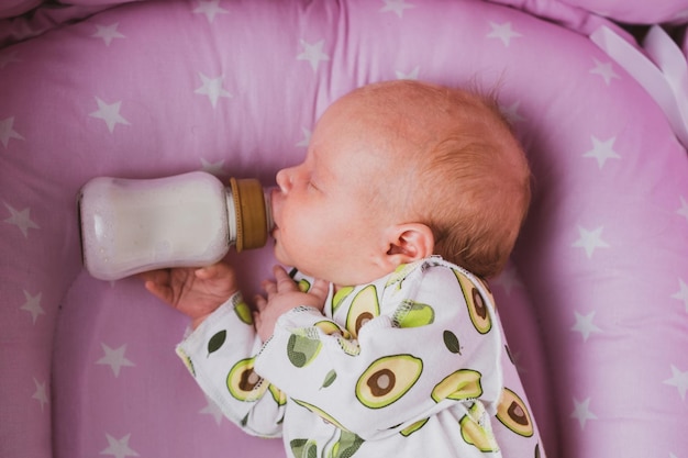 Un neonato beve autonomamente latte o latte artificiale da una bottiglia a casa