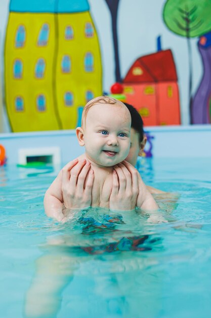 Un neonato nuota in piscina Insegnare ai bambini a nuotare Un bambino impara a nuotare in piscina con un allenatore Un bambino impera a nuotare Sviluppo del bambino