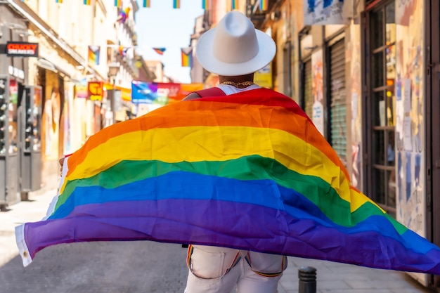 Un nero gay che cammina nella festa dell'orgoglio con una bandiera LGBT sulla schiena