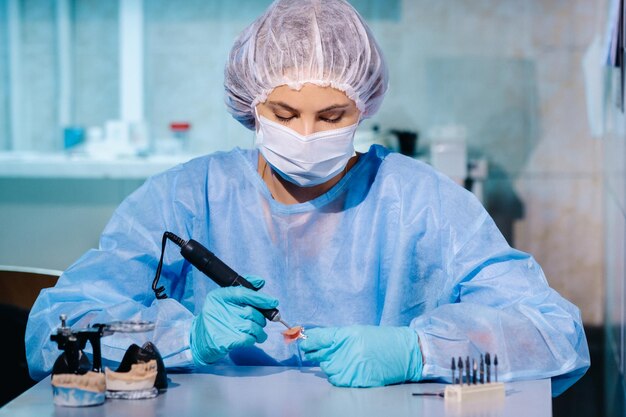 Un odontotecnico in abbigliamento protettivo sta lavorando su un dente protesico nel suo laboratorio