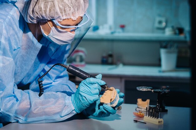 Un odontotecnico in abbigliamento protettivo sta lavorando su un dente protesico nel suo laboratorio