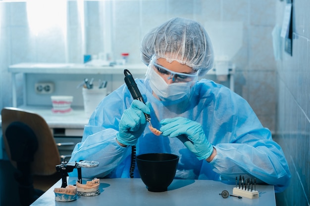 Un odontotecnico mascherato e con guanti lavora su un dente protesico nel suo laboratorio