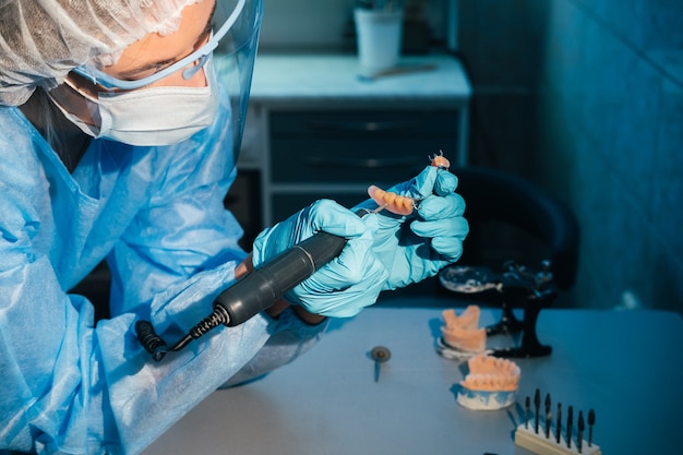 Un odontotecnico mascherato e guantato lavora su un dente protesico nel suo laboratorio.