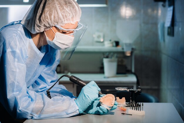 Un odontotecnico mascherato e guantato lavora su un dente protesico nel suo laboratorio.