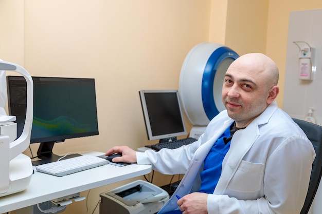 Un oftalmologo maschio sul posto di lavoro al computer guarda la telecamera con un sorriso