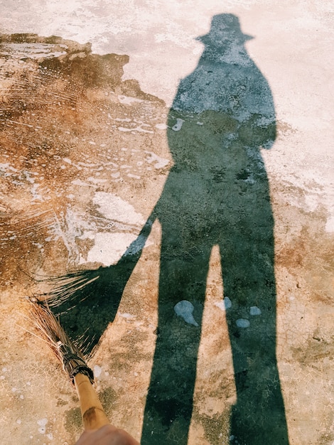 Un&#39;ombra del corpo umano che tiene la scopa in legno pulisce il pavimento di cemento bagnato