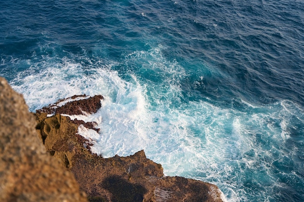 Un'onda dell'oceano che si schianta contro una roccia texturata al tramonto