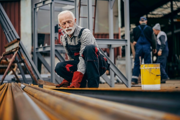 Un operaio anziano dell'industria pesante sta sollevando barre di metallo in una fabbrica metallurgica