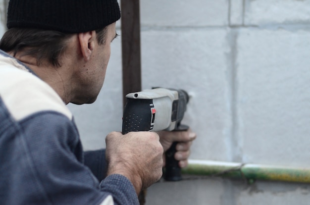 Un operaio anziano fa un buco in una parete di polistirolo per la successiva installazione