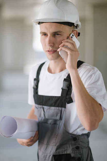 Un operaio edile con la cianografia che parla al telefono