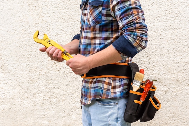 Un operaio edile in una camicia a quadri blu con gli strumenti nella cintura tiene una chiave gialla nelle sue mani.