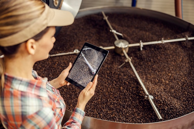 Un operaio femminile del caffè che fotografa il funzionamento della macchina del caffè di torrefazione