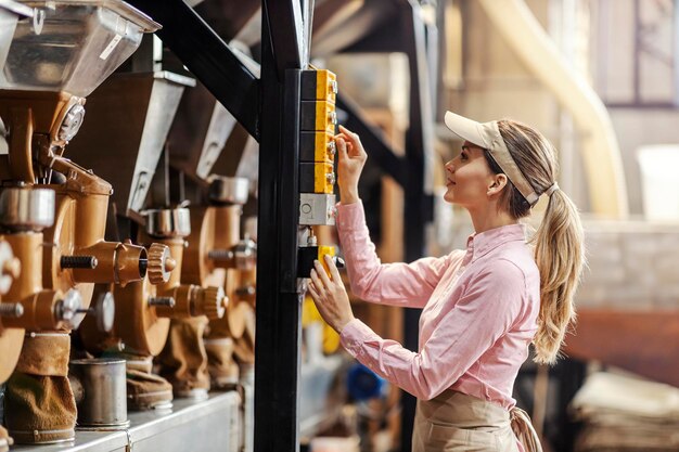 Un operatore femminile che avvia la macchina per la macinazione del caffè in fabbrica