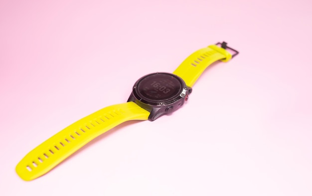 Un orologio giallo con cinturino nero su sfondo rosa.