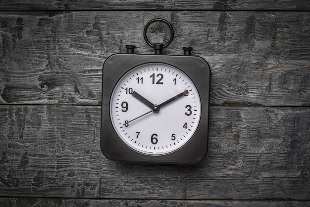 Un orologio nero con quadrante bianco su fondo in legno. Quadrante classico.