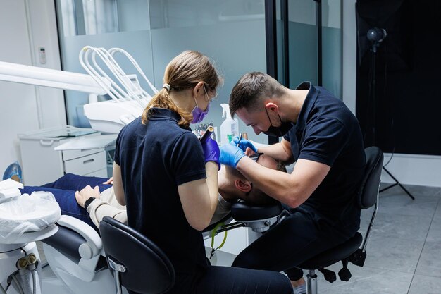 Un ortodontista con un assistente tratta i denti utilizzando strumenti dentali Studio dentistico Trattamento ortodontico dei denti