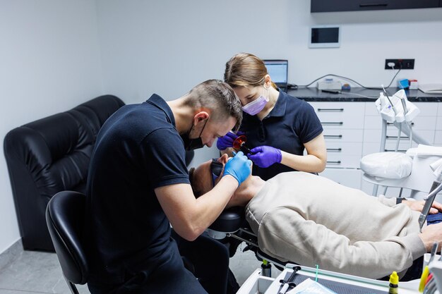 Un ortodontista con un assistente tratta i denti utilizzando strumenti dentali Studio dentistico Trattamento ortodontico dei denti