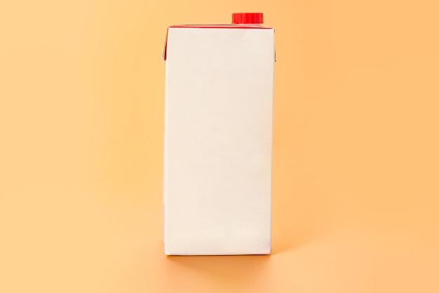 Un pacchetto di carta bianco vuoto bianco di latte con un cappuccio rosso si erge su sfondo arancione Spazio di copia nutrizionale Mockup Mockup Paper Design vuoto