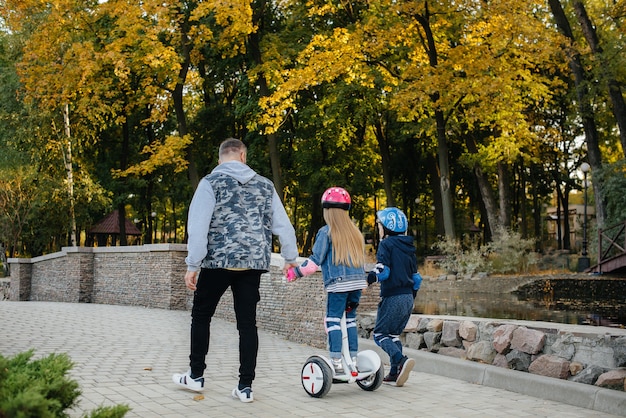 Un padre aiuta e insegna ai suoi figli piccoli a guidare un Segway nel parco durante il tramonto. Vacanza in famiglia nel Parco.