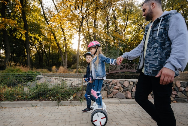 Un padre aiuta e insegna ai suoi figli piccoli a guidare un Segway nel parco durante il tramonto