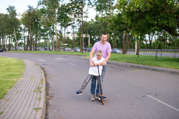 Un padre cavalca suo figlio con una maglietta bianca su uno scooter, il bambino felice allargò le mani