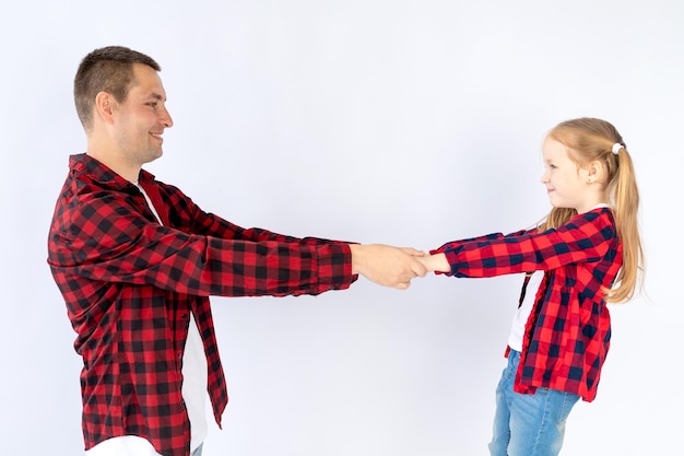 Un padre con una figlia su uno sfondo bianco isolato vuoto in uno studio fotografico in camicie rosse che giocano abbracciando Buona paternità o famiglia