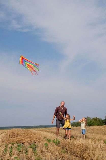 Un padre e le sue figlie lanciano un aquilone arcobaleno in un cielo limpido