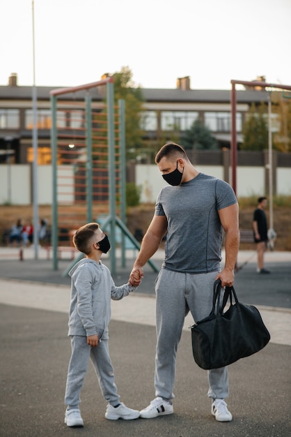 Un padre e un figlio stanno in piedi su un campo sportivo in maschera dopo l'allenamento durante il tramonto.