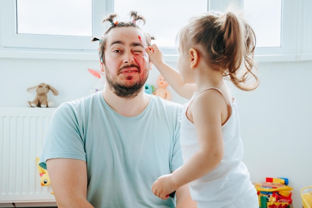 Un padre e una figlia si godono una divertente e creativa sessione di trucco a casa con il papà incoraggiante